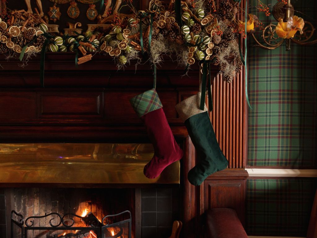 Two Christmas stockings hanging above a fireplace with a mantlepiece topped with foliate decorations