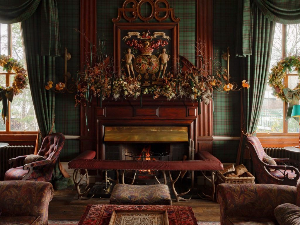 A grand fireplace with windows either side and floral Christmas arrangements on the mantlepiece