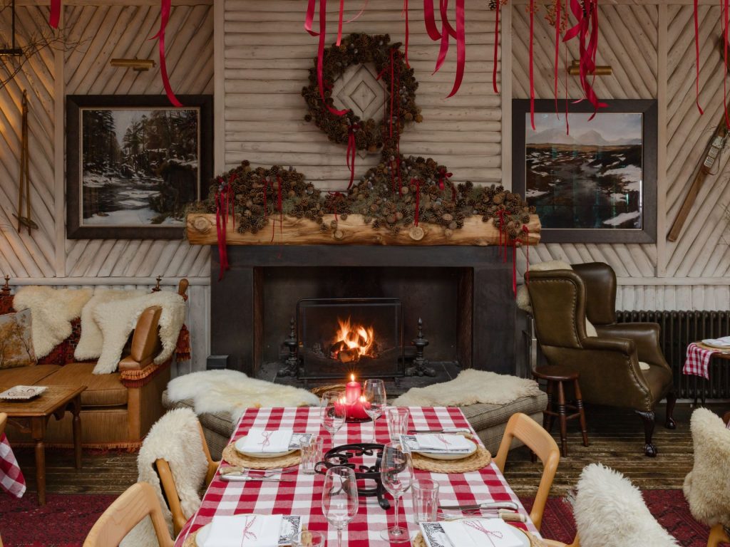A Swiss fondue hut style setting with a fireplace and tables with red gingham tablecloths and sheepskins on chairs