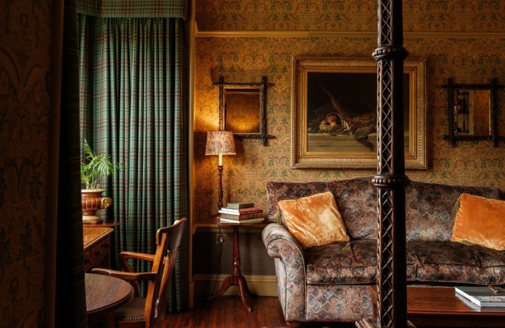 A velvet sofa beside green tartan curtains and antique artworks