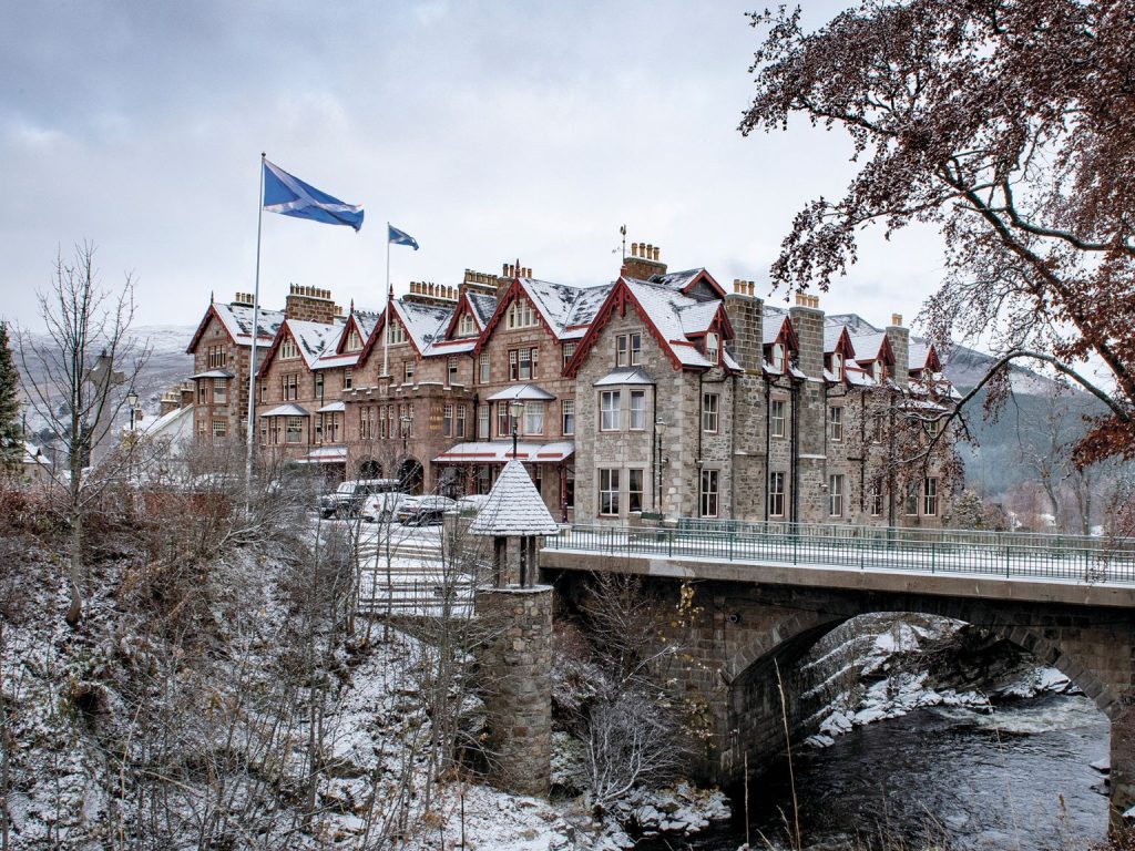 The Victorian Fife Arms hotel in the snow, with a river and bridge in the foreground