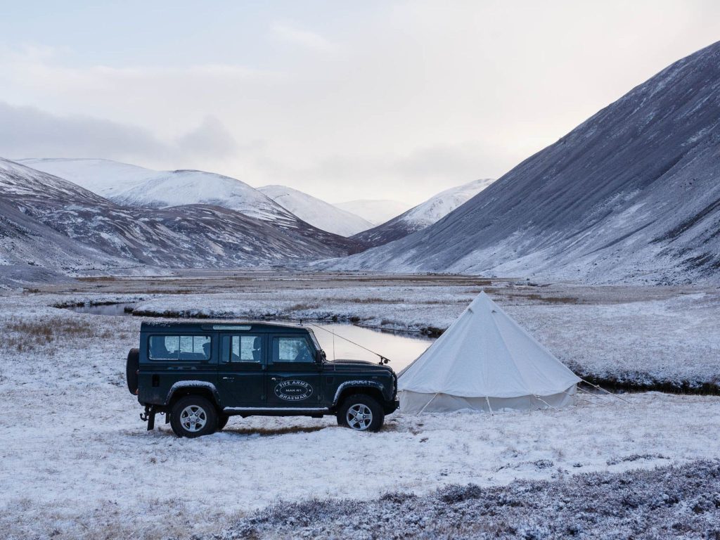 A Land Rover beside a white tent in a snowy glen in the Scottish Highlands