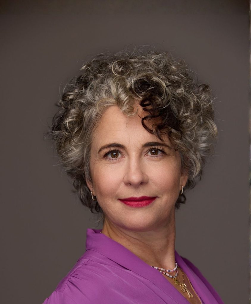 A woman with curly grey hair and a fuschia shirt.