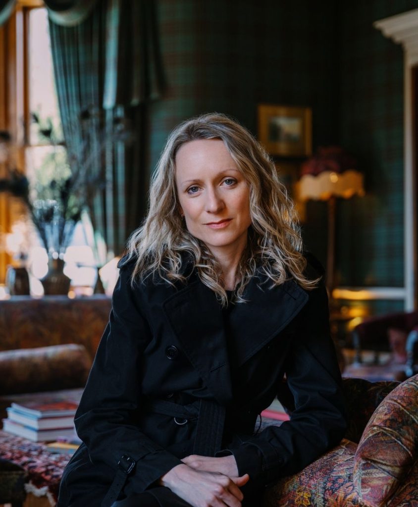 A blonde woman in a black dress in a tartan drawing room