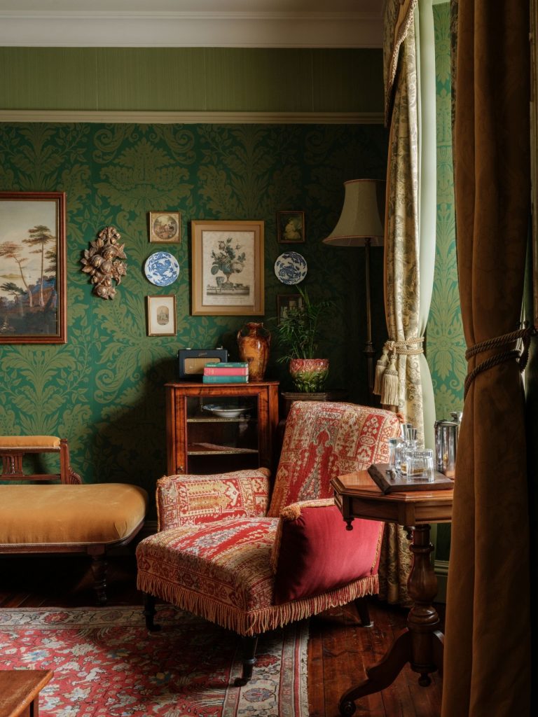 An armchair in a green sitting room with artworks on the walls