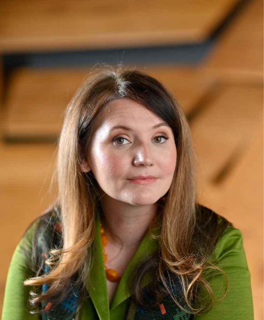 A woman with long brown hair and wearing a green top.