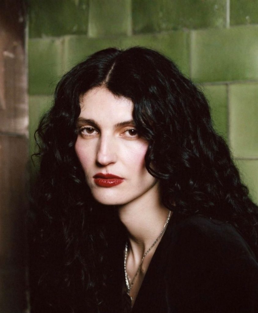 A woman with long dark hair with a green background.