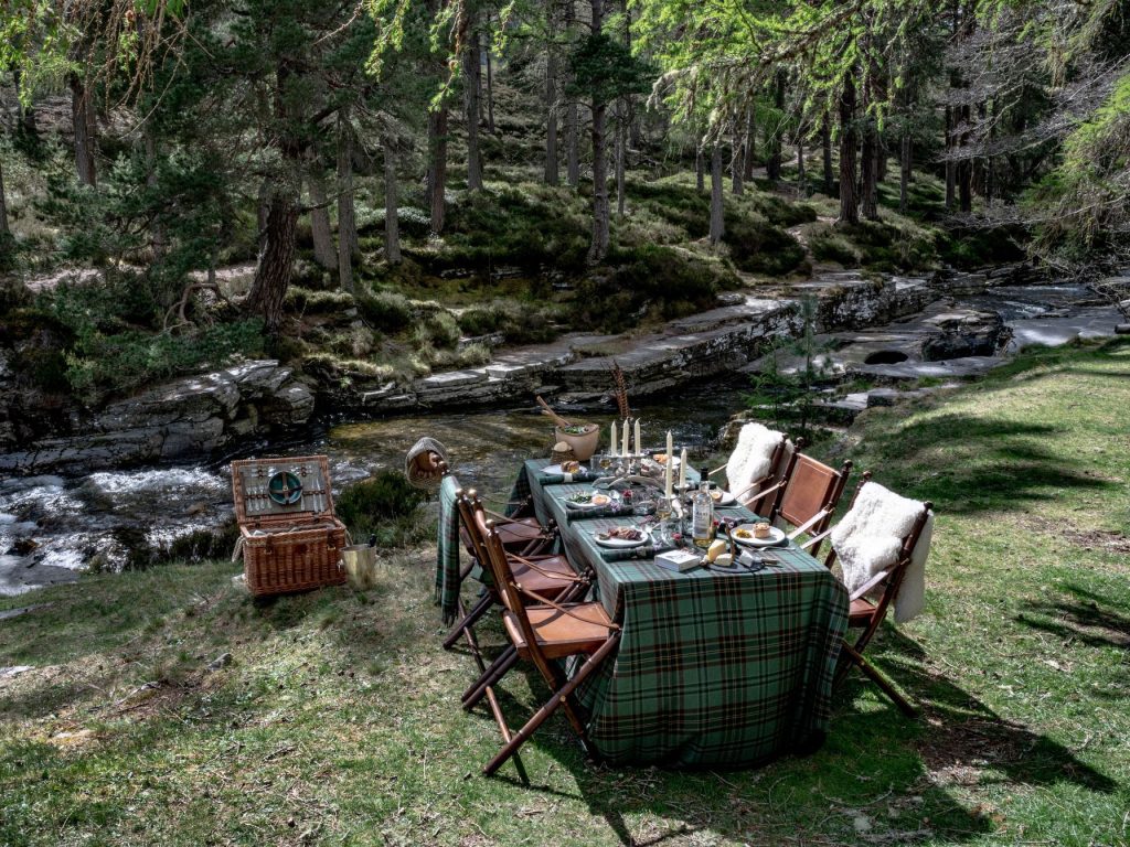 A table with a tartan tablecloth set up beside a river in the Scottish Highlands