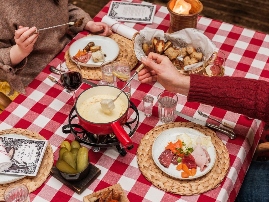 Hands dipping bread in fondue on a table with a gingham tablecloth