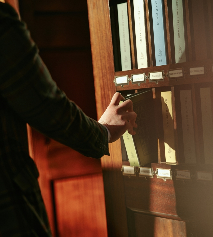A hand selecting a book from a wooden shelf